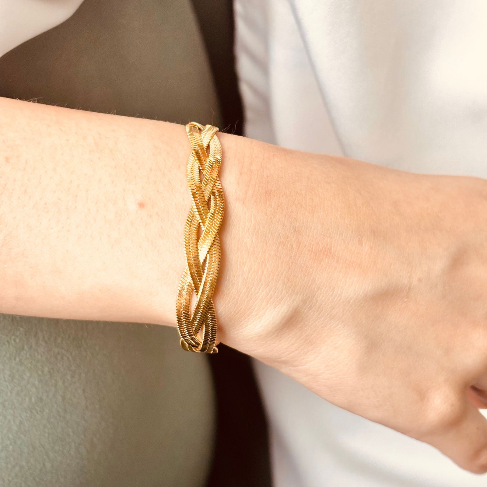 Model's hand close-up of braided gold bracelet highlighting snake chain weave and thickness