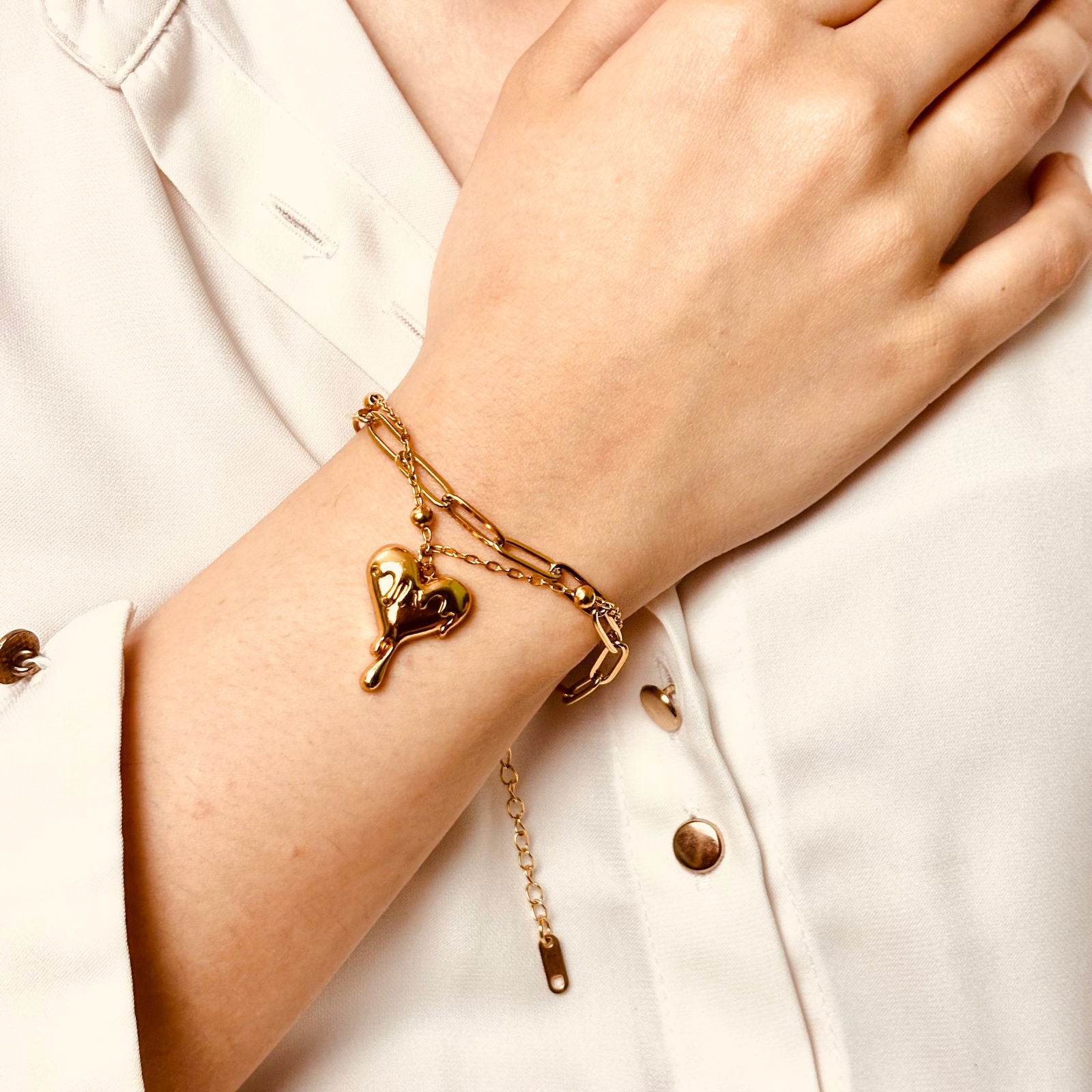 Close-up of model's hand showcasing melting heart charm and layered bracelet chains
