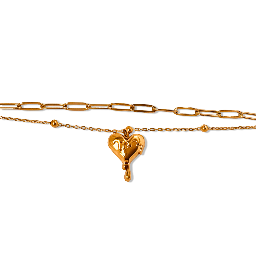 Flat-lay of gold double chain bracelet with melting heart charm