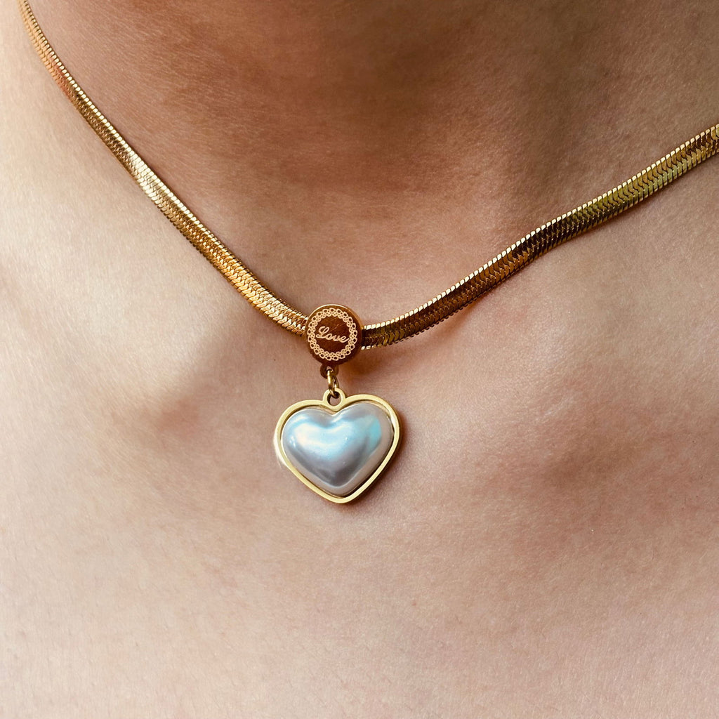 Model's neck close-up showcasing heart-shaped pearl locket and love engraved in the middle of chain - chic minimalistic daily wear accessory