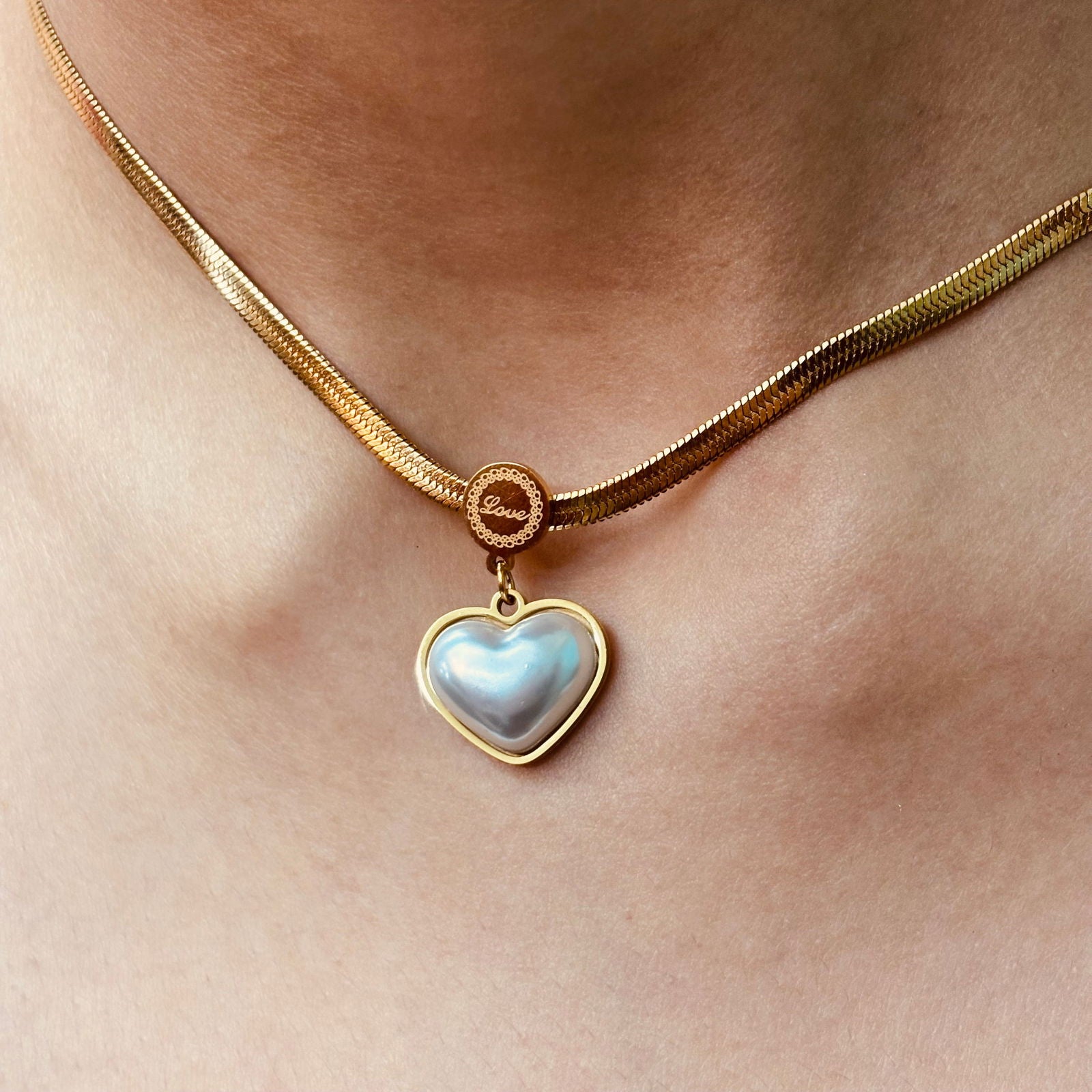 Model's neck close-up showcasing heart-shaped pearl locket and love engraved in the middle of chain - chic minimalistic daily wear accessory