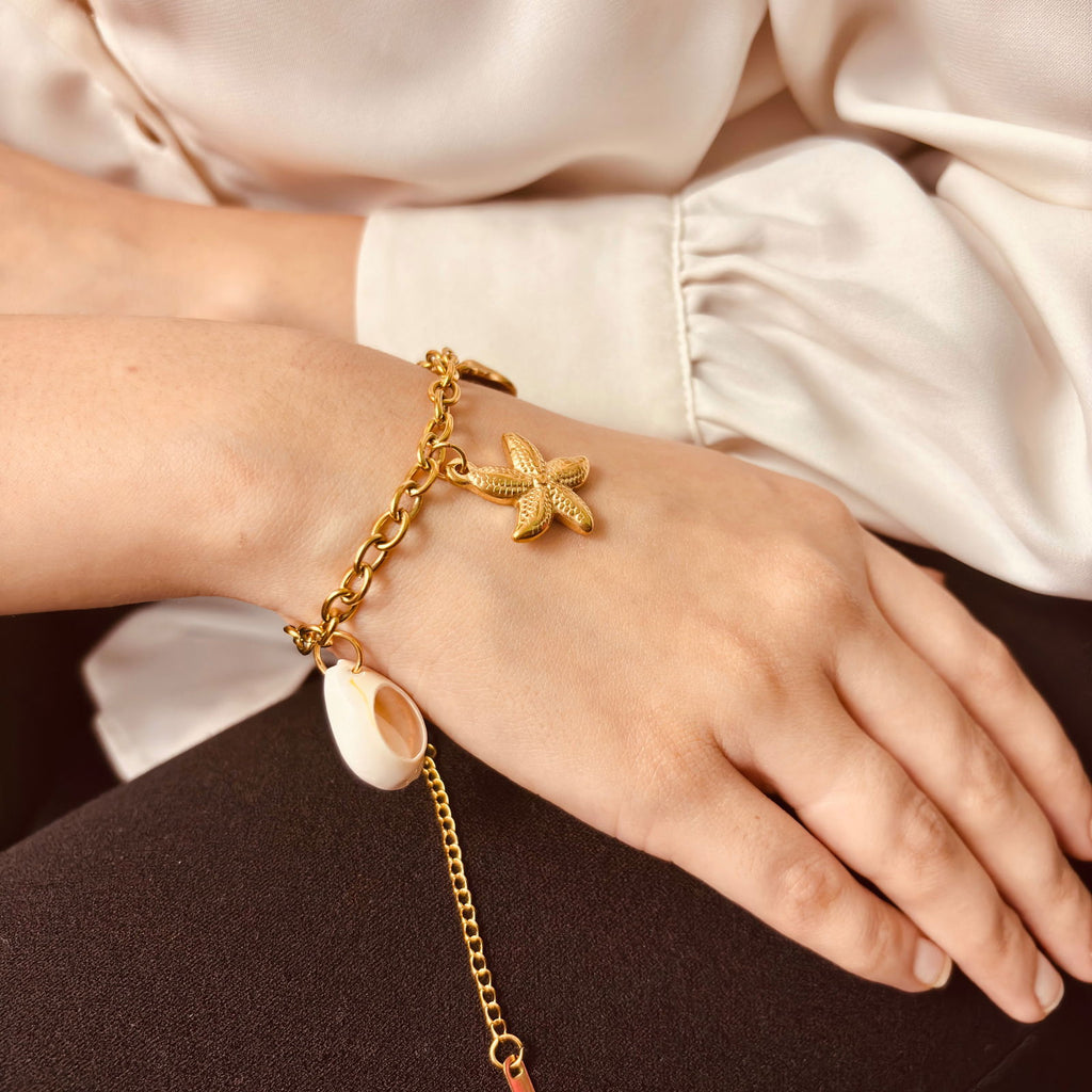 Model's hand showing side view of delicate shell charm bracelet showcasing chain texture - minimalist gold plated bangle birthday gift for her under 2000 - dainty chic starfish and shells gold plated stainless steel bracelet gift ideas under 2000 - hypoallergenic anti‑tarnish gold plated stainless steel bracelet - Rakhi gifts for sister under 2000 - jewelry Raksha Bandhan gifts